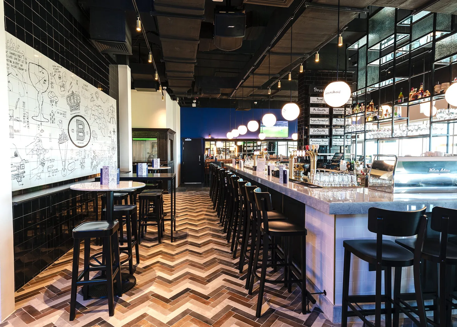 The bar at Le Petit Belge Hamad International Airport, with the sketched tile wall and the Belgian beer board